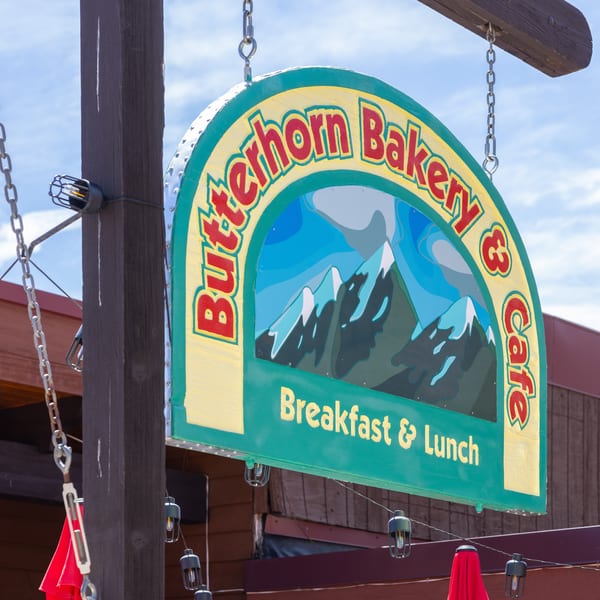 A colorful Butterhorn Bakery & Cafe sign with a mountain graphic hangs from a wooden post.