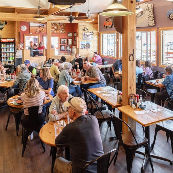 A bustling restaurant interior with many patrons seated at wooden tables, enjoying meals and conversation.