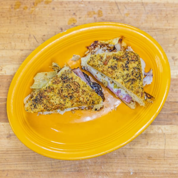 Two halves of a grilled sandwich with meat and cheese, served on a bright yellow plate.