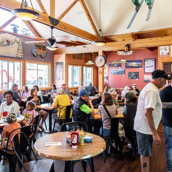 A bustling restaurant interior with many patrons seated at tables, decorated with mountain-themed art and skis.