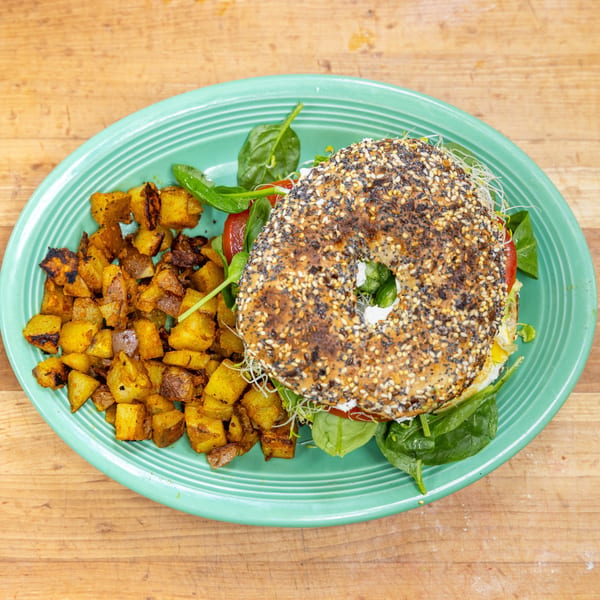Everything bagel sandwich with egg, spinach, tomato, and sprouts, served with roasted potatoes.
