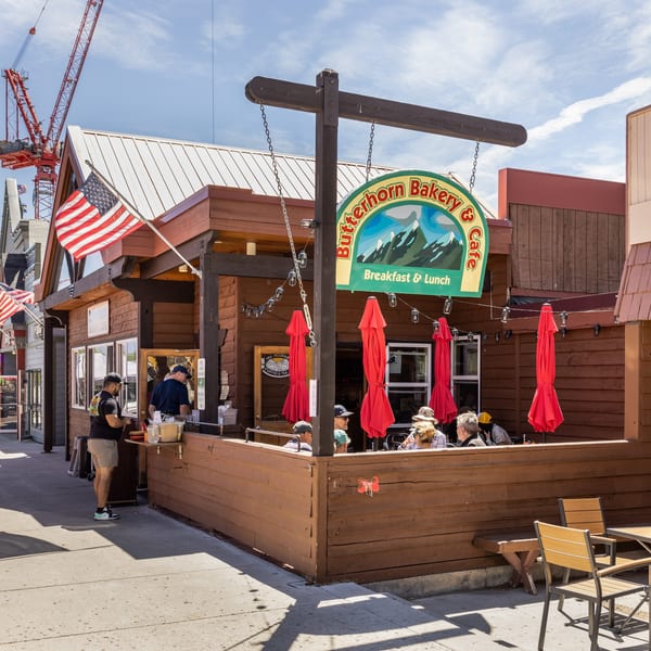 Butterhorn Bakery & Cafe with outdoor seating, red umbrellas, and people dining on a sunny day.