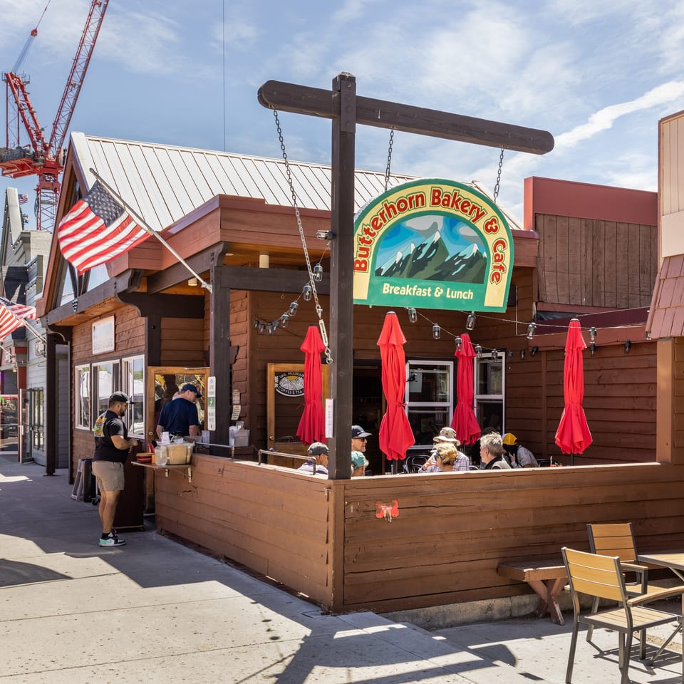 Butterhorn Bakery & Cafe with outdoor seating, red umbrellas, and people dining on a sunny day.