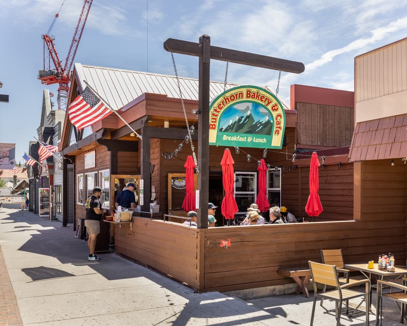 Butterhorn Bakery & Cafe with outdoor seating, red umbrellas, and people dining on a sunny day.