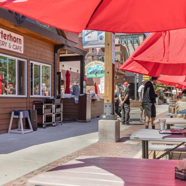 Outdoor dining area of Butterhorn Bakery & Cafe with red umbrellas, picnic tables, and people.