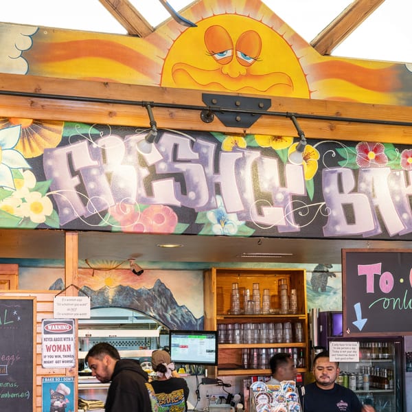 A vibrant, colorful mural with "FRESH BAKED" in graffiti-style letters above a bustling restaurant counter.