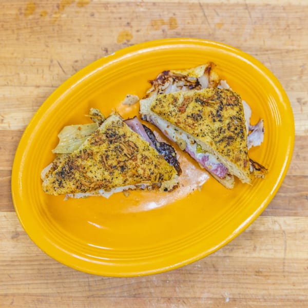 Two halves of a grilled sandwich with meat and cheese, served on a bright yellow plate.