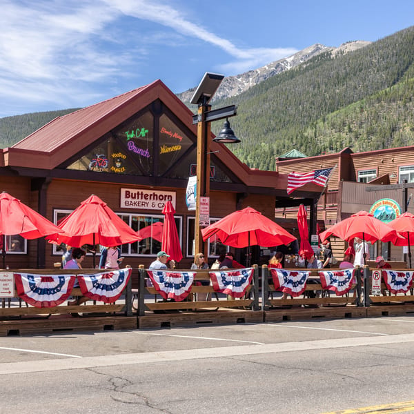 Butterhorn Bakery & Cafe with outdoor patio seating under red umbrellas, backed by mountains.
