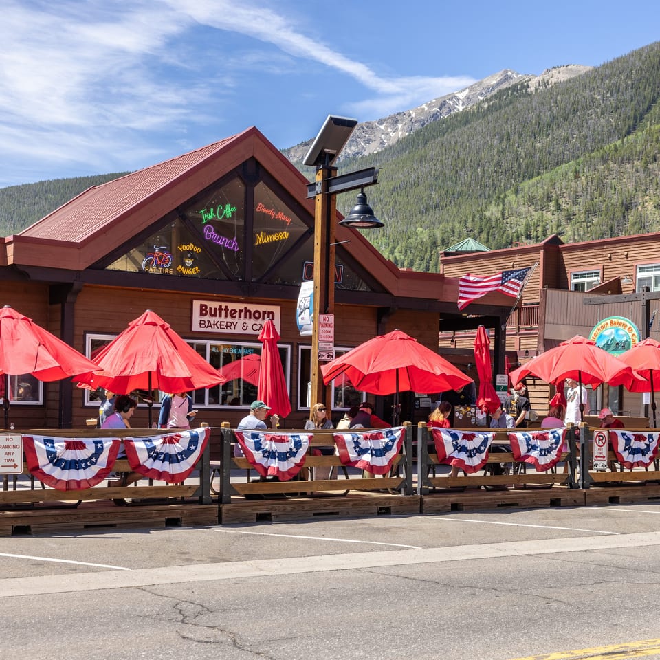 Butterhorn Bakery & Cafe with outdoor patio seating under red umbrellas, backed by mountains.