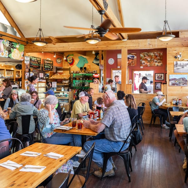 A busy, rustic restaurant interior with many patrons seated at wooden tables, enjoying meals and conversation.