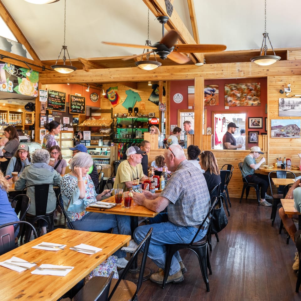 A busy, rustic restaurant interior with many patrons seated at wooden tables, enjoying meals and conversation.