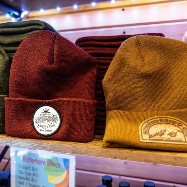 Butterhorn Bakery & Cafe branded beanies in red and mustard yellow on a wooden shelf.